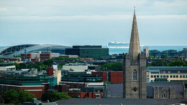 em-dublin-20261025am Daylight view across the Dublin city skyline with the spire of Saint Patrick's Cathedral and Dublin Bay beyond