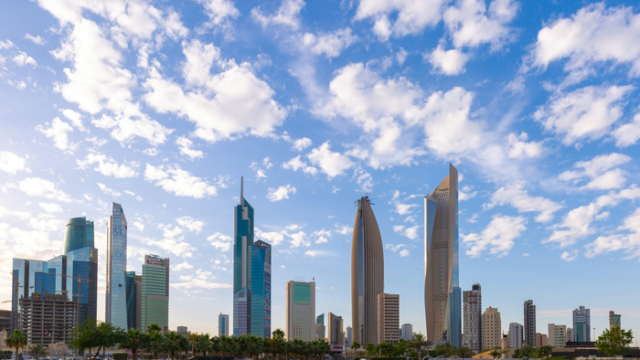 The Kuwait City skyline photographed in daylight under broken white cloud